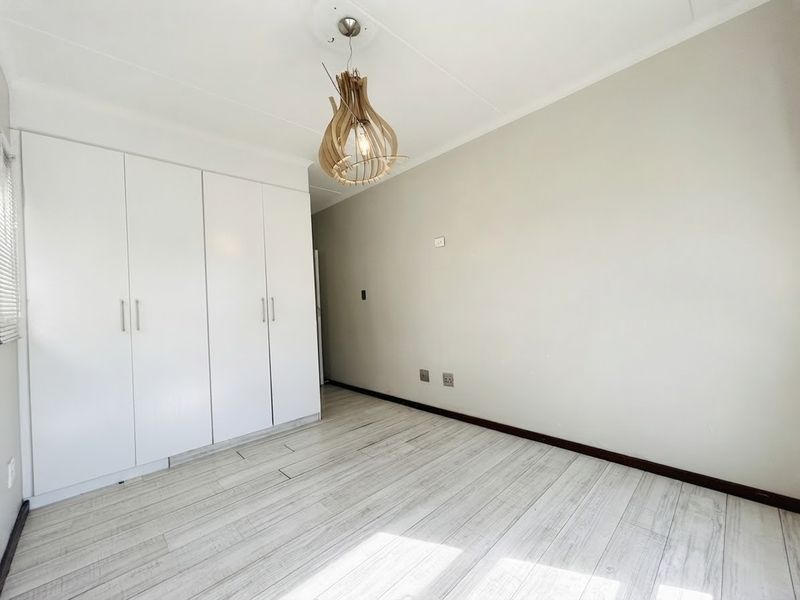 A bright, empty bedroom featuring light-toned laminate flooring, neutral walls, and ample built-in cupboard storage.