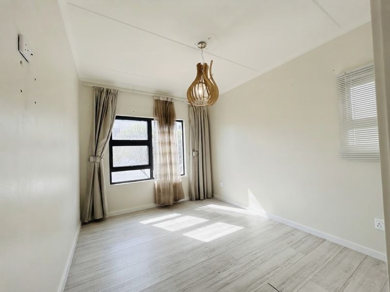 A bright, empty bedroom featuring light-toned laminate flooring, aluminium window frames, and neutral wall finishes, ready for personalization.