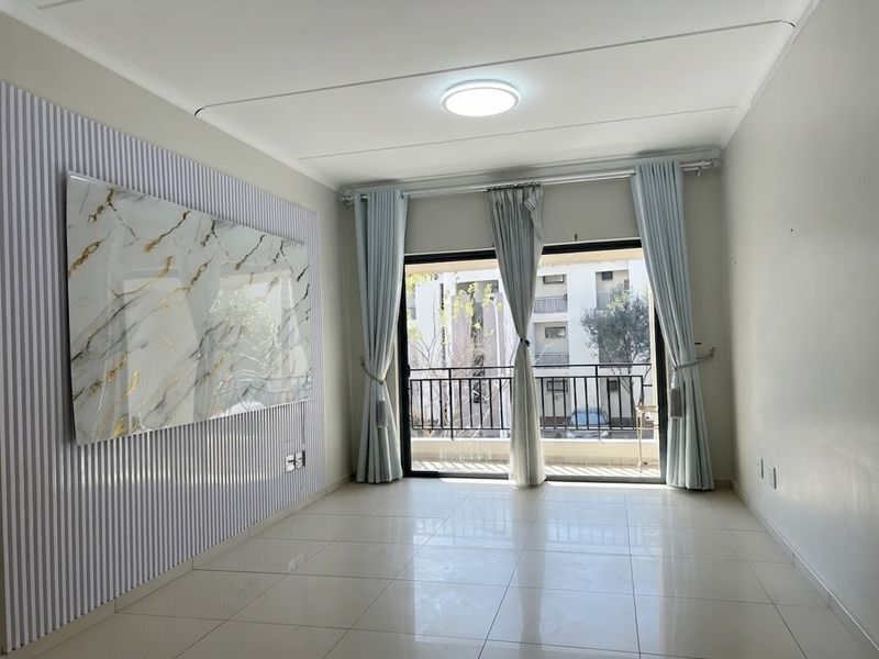 Bright and spacious living area featuring neutral tiled flooring, decorative wall paneling, and a sliding glass door leading to a private balcony.