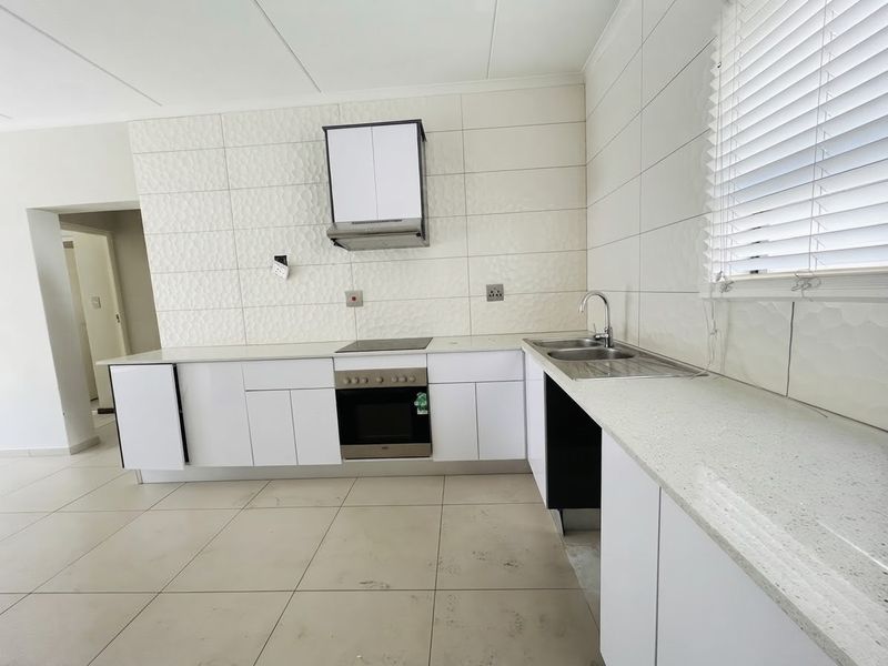A functional kitchen featuring white cabinetry, stone countertops, integrated oven and hob, and a tiled splashback. The space is clean and ready for use.