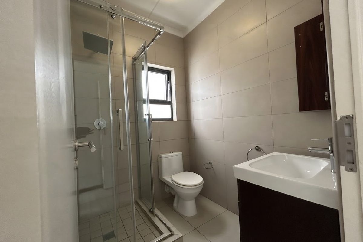 A clean, modern bathroom featuring a glass-enclosed shower, a vanity unit with a basin, and neutral wall and floor tiling.