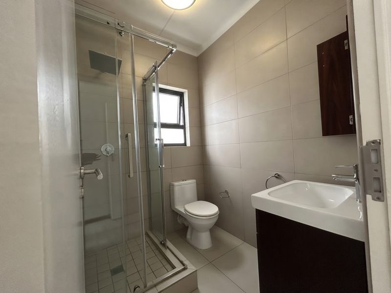 A clean, modern bathroom featuring a glass-enclosed shower, a vanity unit with a basin, and neutral wall and floor tiling.