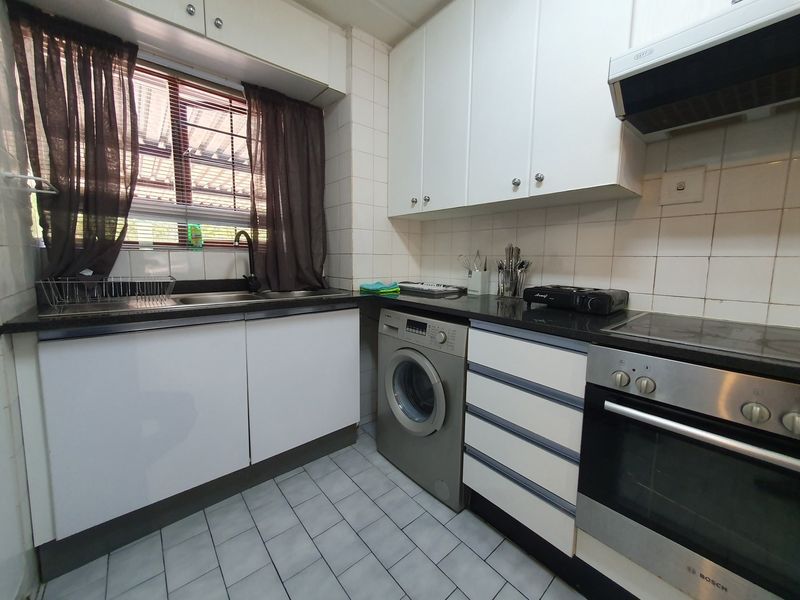 Functional kitchen featuring white cabinetry, black granite countertops, built-in oven, electric hob, extractor fan, and tiled finishes.