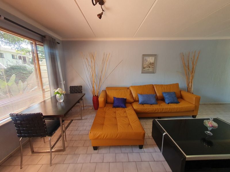 A living room area featuring tiled flooring, a large window with blinds, and a ceiling-mounted light fixture.