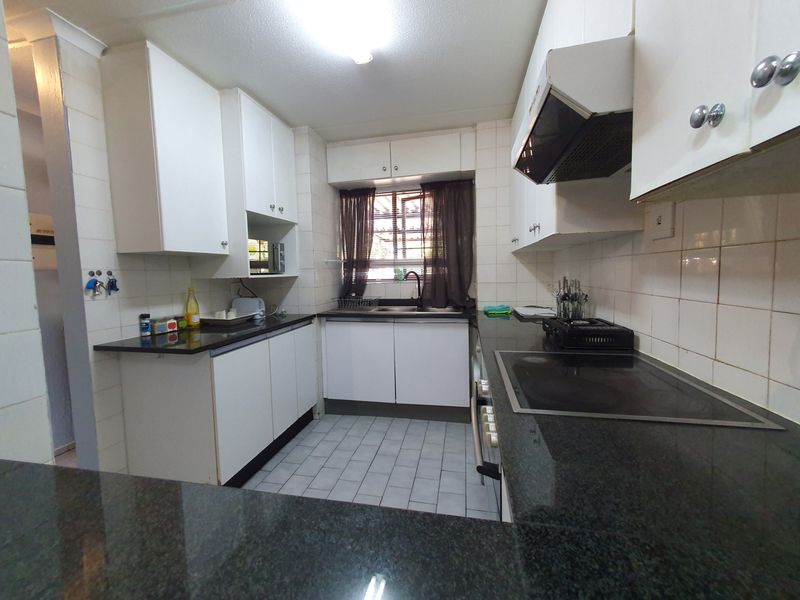 A functional kitchen featuring white cabinetry, dark granite countertops, an integrated electric hob, extractor fan, and tiled finishes throughout.