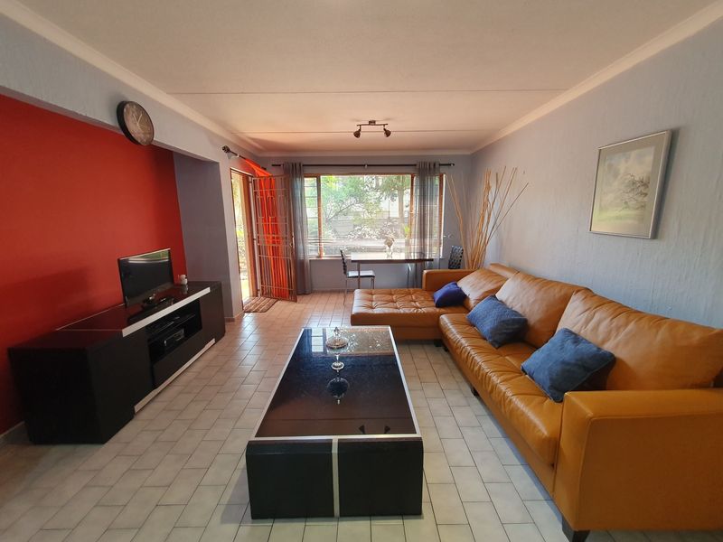 A spacious living room featuring tiled flooring, cove cornicing, and large windows that provide natural light and access to the exterior.