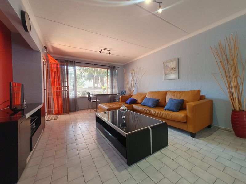 A spacious living room featuring tiled flooring, ceiling track lighting, and a large window with an integrated security gate.