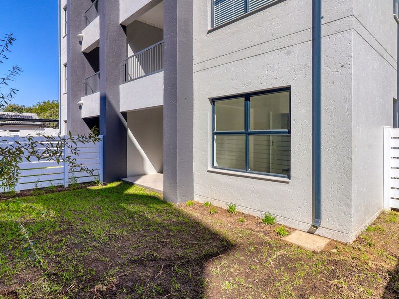 Rear view of the apartment building featuring a private ground floor patio area and a small garden space with perimeter fencing.