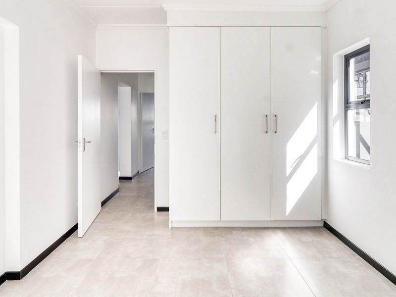 A bright, empty bedroom featuring neutral tiled flooring, built-in cupboards, and clean white finishes, offering a versatile space ready for personalization.