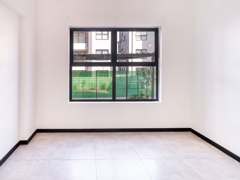 A bright, empty bedroom featuring neutral tiled flooring, crisp white walls, and a large window with a black frame.