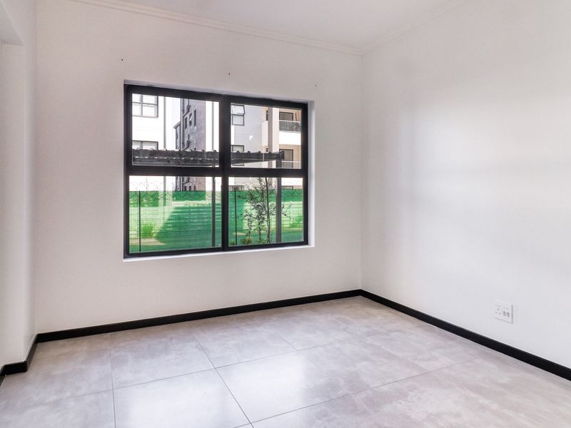 A bright, empty bedroom featuring neutral tiled flooring, clean white walls, and modern black-framed windows.