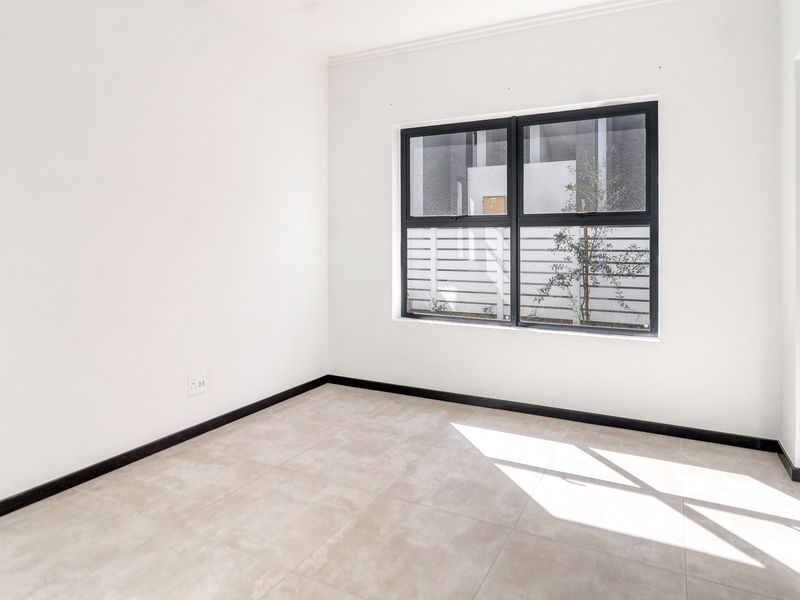 A bright, empty bedroom featuring neutral tiled flooring, modern dark aluminium window frames, and clean white walls, ready for personalization.
