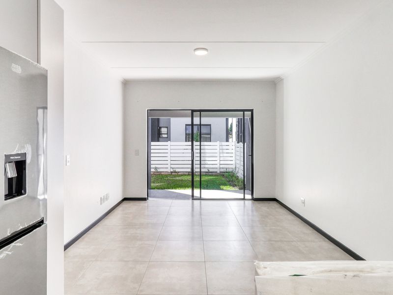 A bright, empty open-plan living area featuring neutral tiled flooring and a sliding glass door providing direct access to the rear garden.