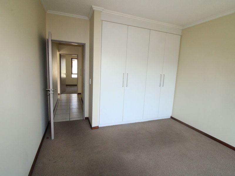 A clean, empty bedroom featuring neutral walls, carpeted flooring, and ample built-in cupboard storage space.