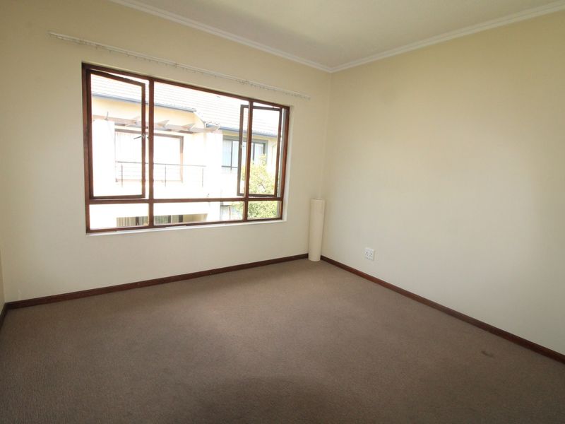 A vacant bedroom featuring neutral walls, carpeted flooring, and large timber-framed windows allowing for natural light.