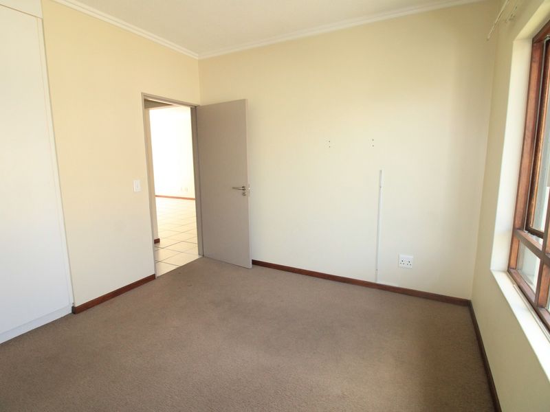An empty bedroom featuring neutral walls, carpet flooring, a built-in wardrobe, and a timber-framed window allowing natural light.