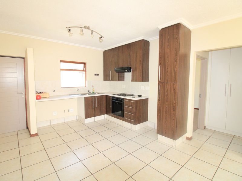 A functional kitchen featuring dark wood cabinetry, built-in oven and hob, extractor fan, and tiled flooring, offering a clean and practical workspace.