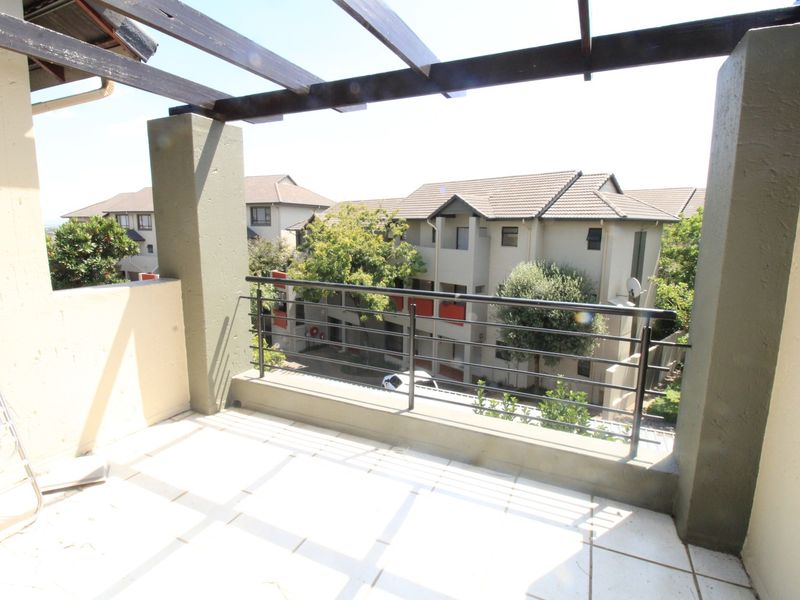 A covered balcony featuring a timber pergola, metal balustrade, and tiled flooring, offering an outdoor space with views of the surrounding apartment complex.