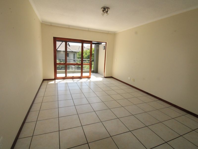 An empty, well-lit living room featuring neutral tiled flooring and a large sliding glass door providing access to an outdoor balcony area.