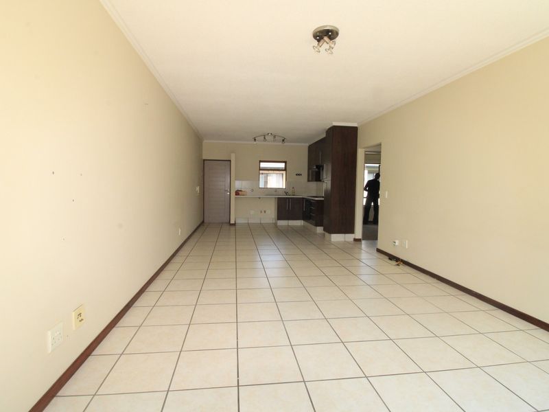 Spacious open-plan living and kitchen area featuring neutral tiled flooring and built-in cabinetry, offering a versatile layout for modern apartment living.