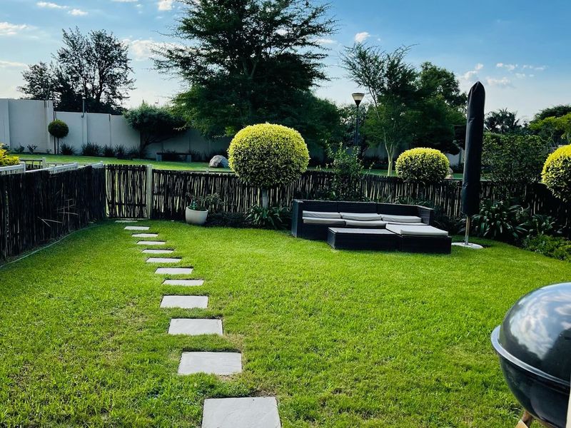 A well-maintained private rear garden featuring a lush lawn, stone pathway, and a tiled patio area, enclosed by a timber fence.