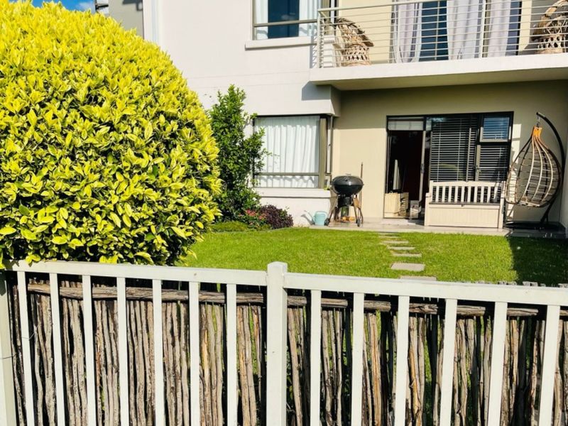 Rear view of the apartment building featuring a private garden, paved patio area, and an upper-level balcony with metal railings.