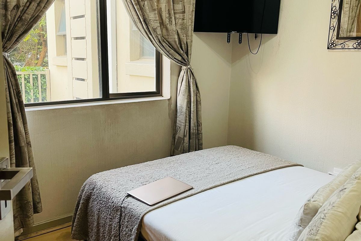 A compact bedroom featuring laminate flooring, a window with curtains, and a wall-mounted television bracket.