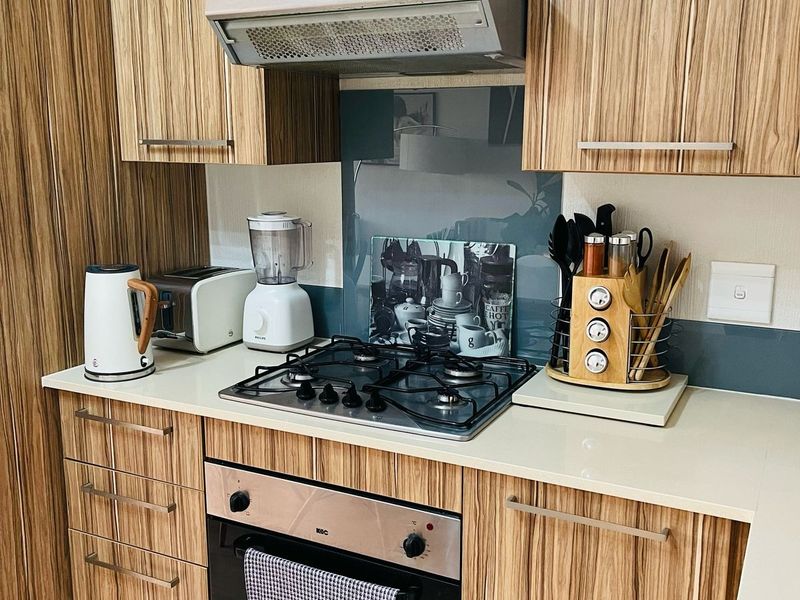 A well-maintained kitchen featuring wood-grain cabinetry, a gas hob, built-in oven, extractor fan, and a modern glass splashback.