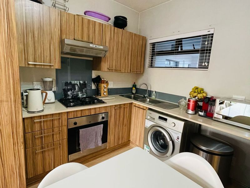 Compact kitchen featuring wood-grain cabinetry, built-in oven, gas hob, extractor fan, and an integrated washing machine with a stainless steel sink.