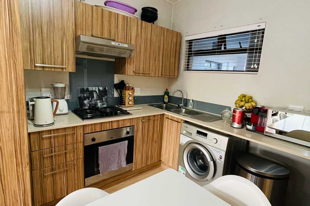 Compact kitchen featuring wood-grain cabinetry, built-in oven, gas hob, extractor fan, and an integrated washing machine with a stainless steel sink.