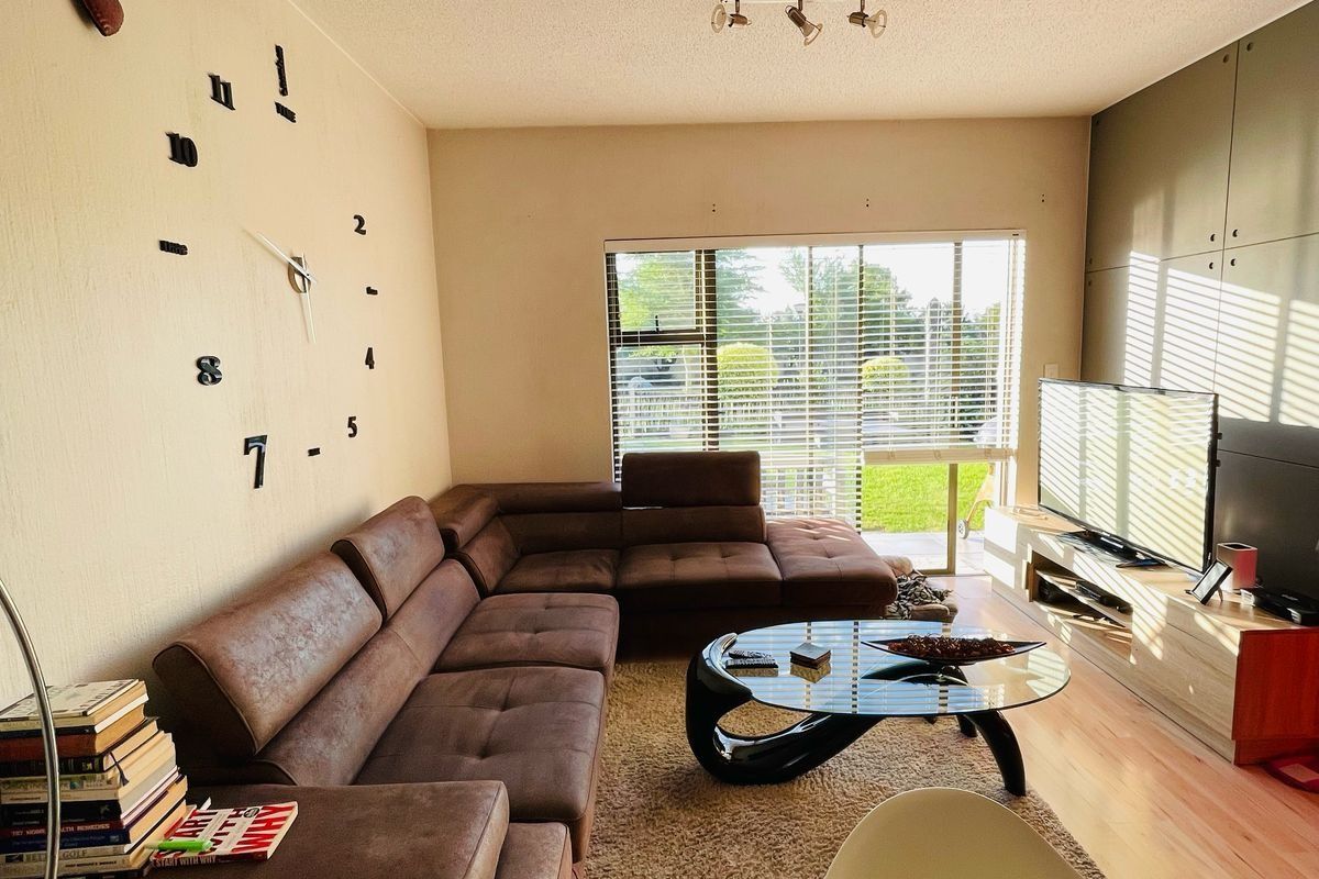 A comfortable living room featuring laminate flooring, track lighting, and large windows with venetian blinds, offering a bright and functional space.