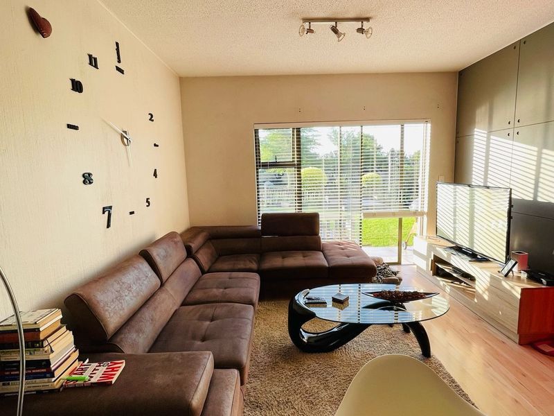A comfortable living room featuring laminate flooring, track lighting, and large windows with venetian blinds, offering a bright and functional space.