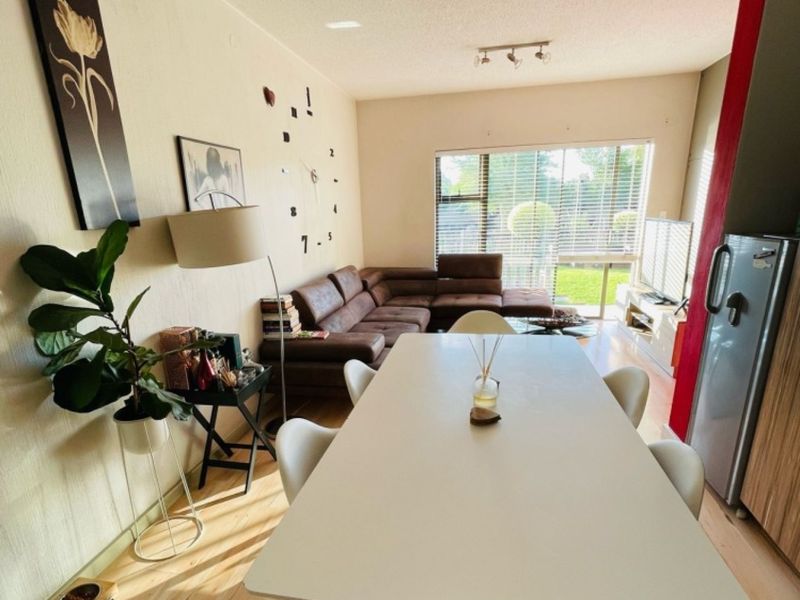 Open plan living and dining area featuring light laminate flooring, neutral walls, and large windows providing natural light.