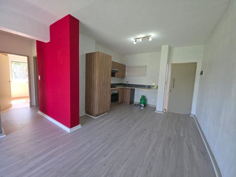 Open-plan living area featuring a compact kitchen with built-in cabinetry, oven, hob, and extractor fan, finished with light-toned laminate flooring.