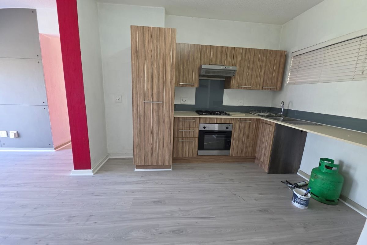 A functional kitchen featuring wood-look cabinetry, built-in oven, gas hob, and extractor fan, finished with modern laminate flooring.