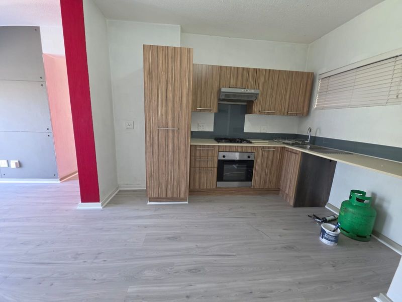 A functional kitchen featuring wood-look cabinetry, built-in oven, gas hob, and extractor fan, finished with modern laminate flooring.