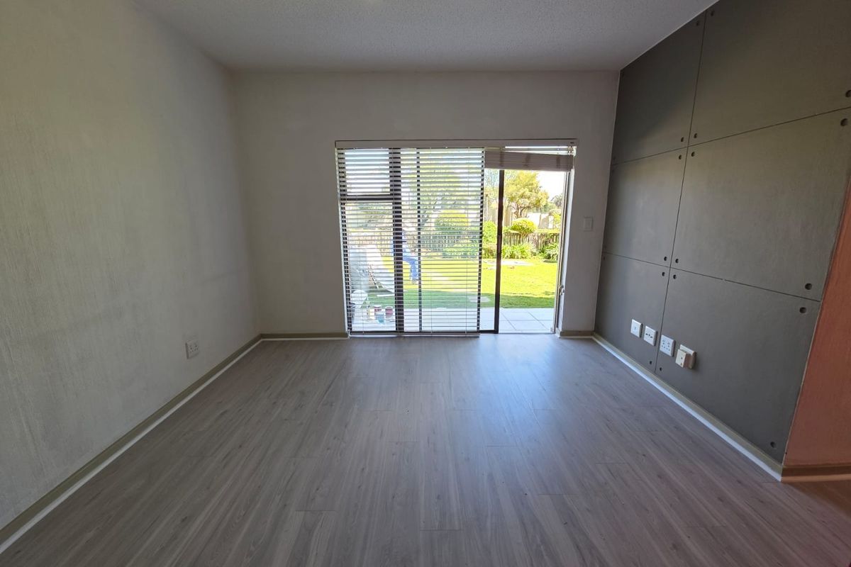 An empty living room featuring modern laminate flooring, a decorative feature wall, and a sliding glass door providing direct access to the garden.