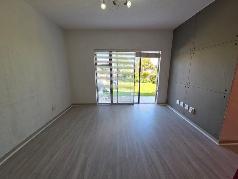 An empty living room featuring modern laminate flooring, a decorative feature wall, and a sliding glass door providing direct access to the garden.