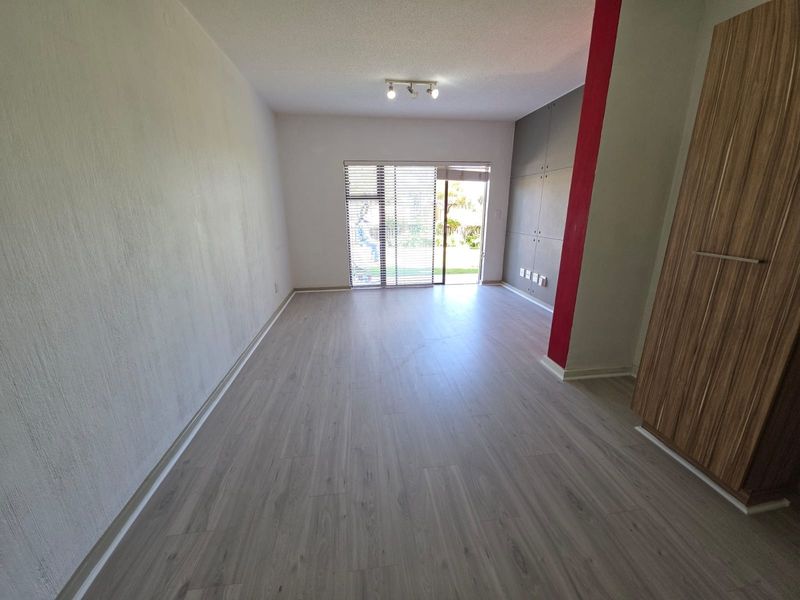 A bright, empty living area featuring modern laminate flooring, built-in storage cabinetry, and a sliding glass door providing access to the outdoor space.