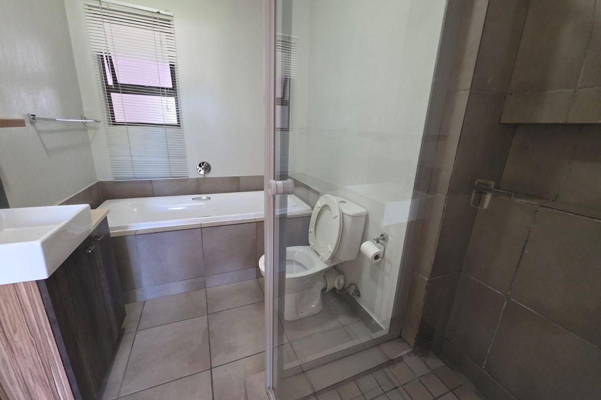 A modern bathroom featuring a built-in bathtub, a separate glass-enclosed shower, a vanity unit with a basin, and neutral floor-to-ceiling tiling.