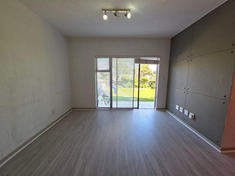 An empty living room featuring modern laminate flooring, a feature wall with paneling, track lighting, and a sliding glass door leading to the garden.