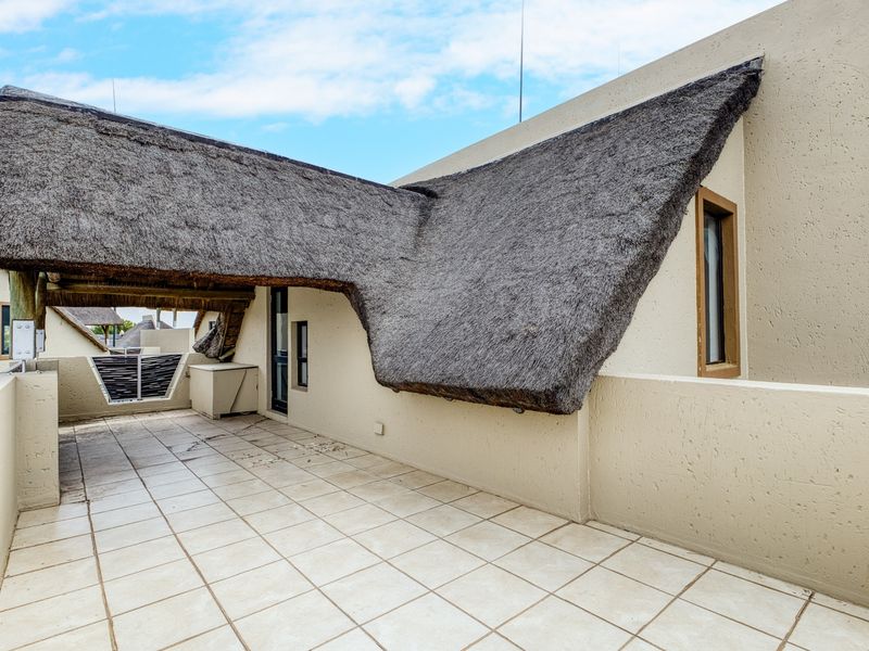 A spacious outdoor balcony featuring a traditional thatched roof covering and tiled flooring, offering a unique architectural aesthetic.