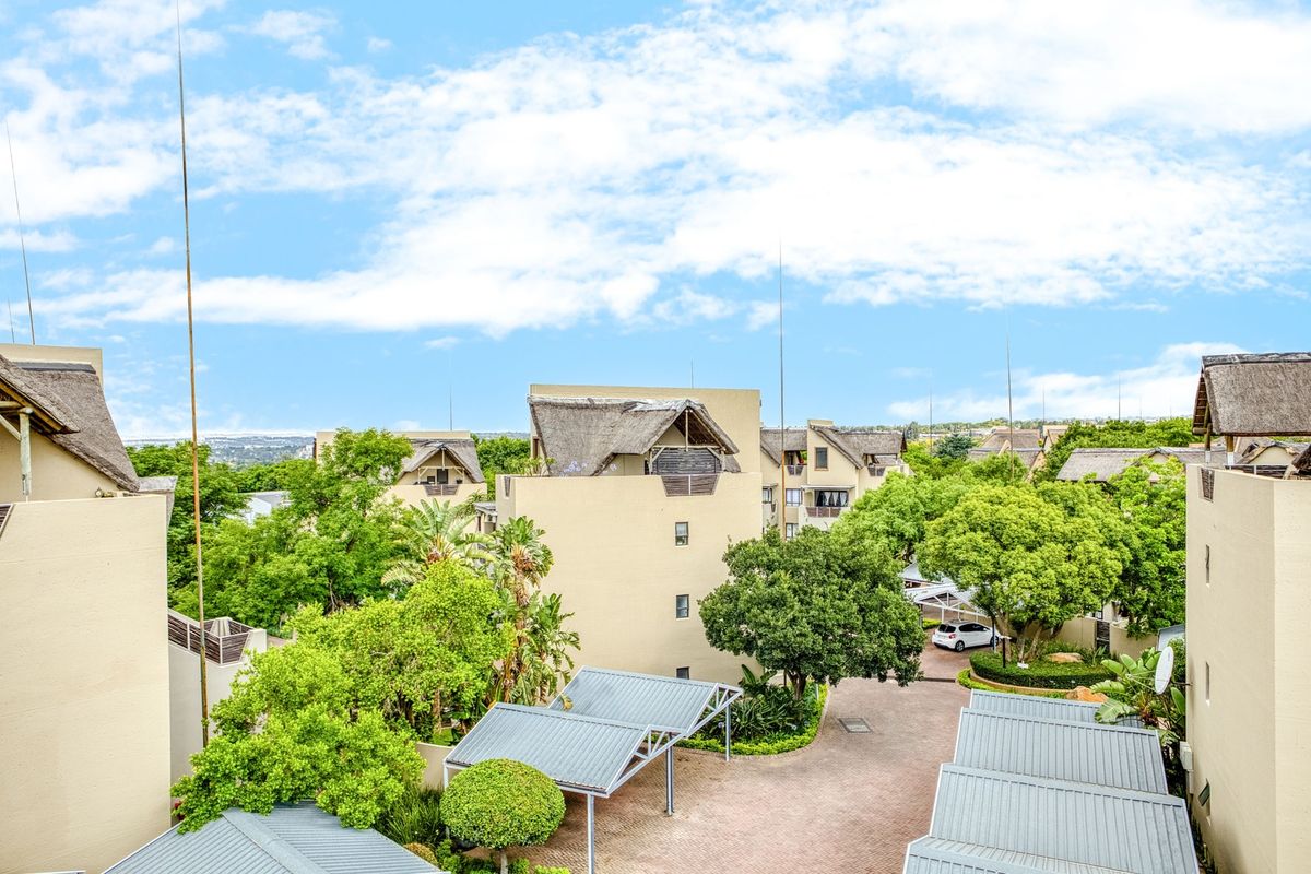 An elevated aerial view of the apartment complex featuring thatched roof buildings, paved driveways, carports, and established green landscaping.