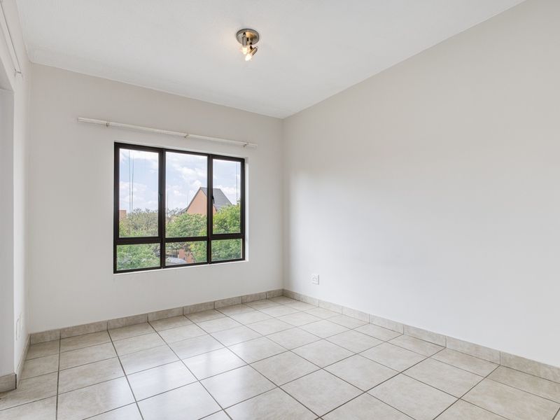 A bright, empty bedroom featuring neutral tiled flooring, clean white walls, and a large aluminium-framed window providing natural light.