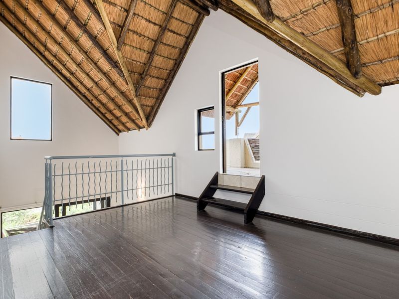 Spacious loft-style living area featuring high exposed thatch ceilings, dark timber flooring, and direct access to an outdoor balcony.