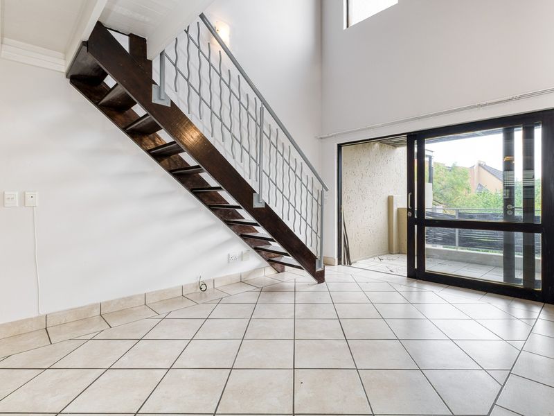 Spacious double-volume living area featuring a wooden staircase with metal balustrade, tiled flooring, and large sliding doors leading to an outdoor balcony.