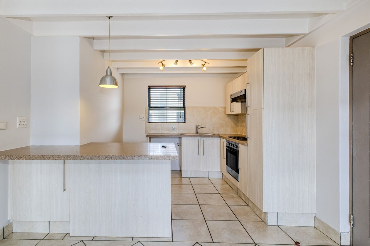 A clean, functional kitchen featuring light-toned cabinetry, laminate countertops, built-in oven and hob, tiled flooring, and exposed beam ceilings.