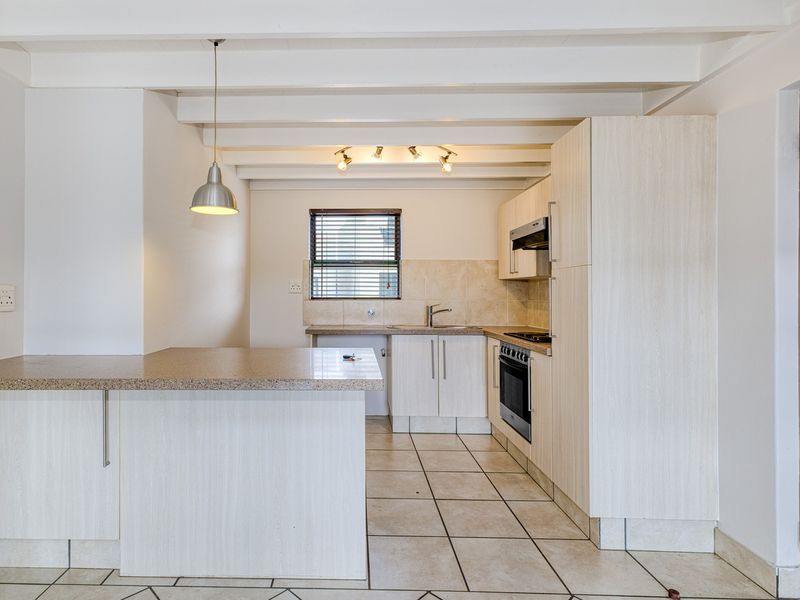 A clean, functional kitchen featuring light-toned cabinetry, laminate countertops, built-in oven and hob, tiled flooring, and exposed beam ceilings.