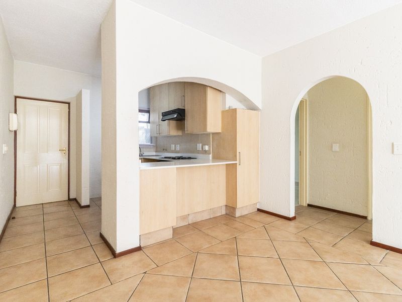 An open-plan living area featuring ceramic floor tiles, arched architectural details, and a compact kitchen with built-in cabinetry and a hob.
