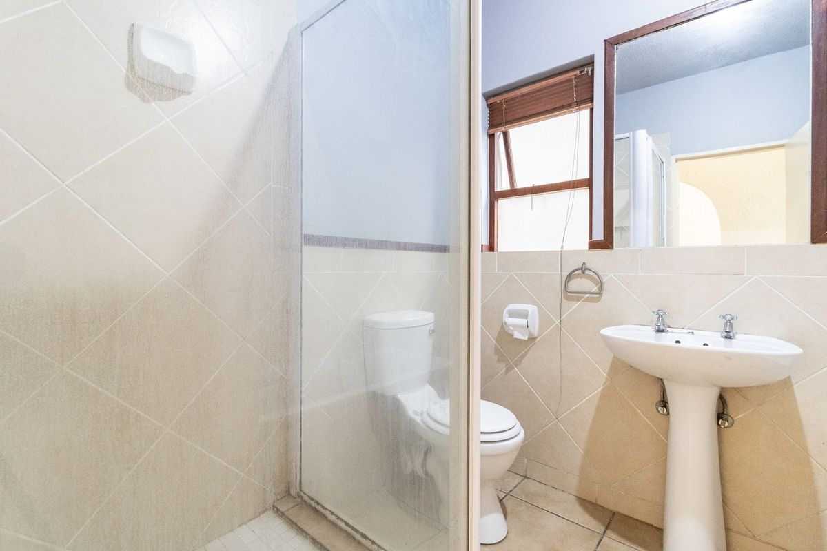 A functional bathroom featuring a pedestal basin, toilet, and a glass-enclosed shower with neutral wall and floor tiling.